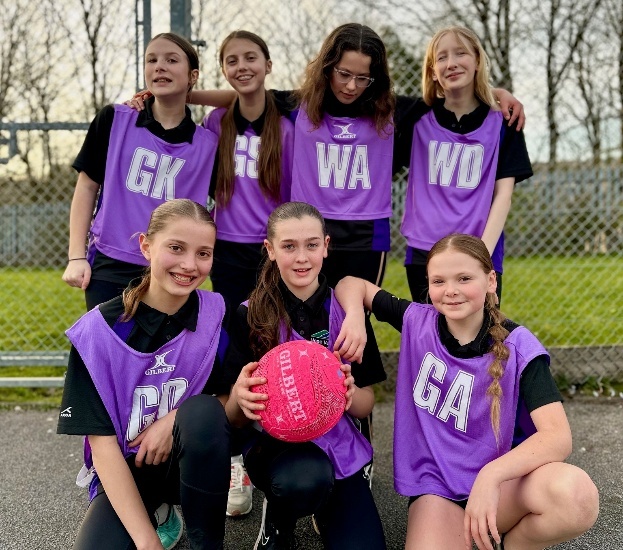 Year 7 Netball Team in purple bibs, smiling on the court